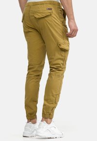 Pantaloni cargo kaki cu manșete elastice la gleznă, mai multe buzunare și un material texturat. Prezintă o etichetă la talie, proiectați pentru confort și utilitate.