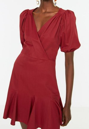 Rode wikkeljurk met pofmouwen, een V-hals en een uitlopende zoom. Gemaakt van gladde stof, met subtiele plooien en een getailleerde taille.
