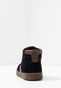 Navy modré semišové kotníkové boty s hnědým koženým akcentem na patě. Mají texturovanou gumovou podrážku a kontrastní švy.