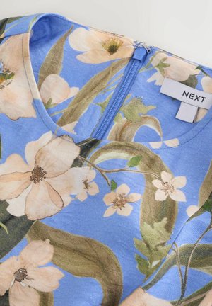 Blus med blommönster på ljusblå bas, mjukt tyg, V-ringning och en blå dragkedja bak med en vit etikett märkt "NEXT".