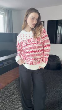 Pull en tricot blanc avec motifs géométriques rouges. Coupe oversize avec poignets et ourlet côtelés. Porté avec un pantalon noir ample.