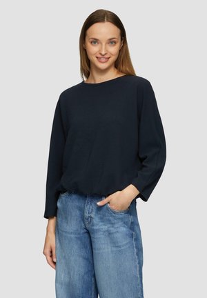 Marineblauw, geribbelde top met lange mouwen en een brede halslijn, ontspannen pasvorm en een licht cropped zoom, gedragen met lichtblauwe, hooghartige jeans.