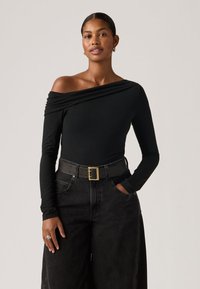 Μαύρο κορμάκι με μακριά μανίκια και ανοιχτούς ώμους, συνδυασμένο με ψηλόμεσα μαύρα τζιν και φαρδύ μαύρο ζωνάρι με χρυσή αγκράφα.