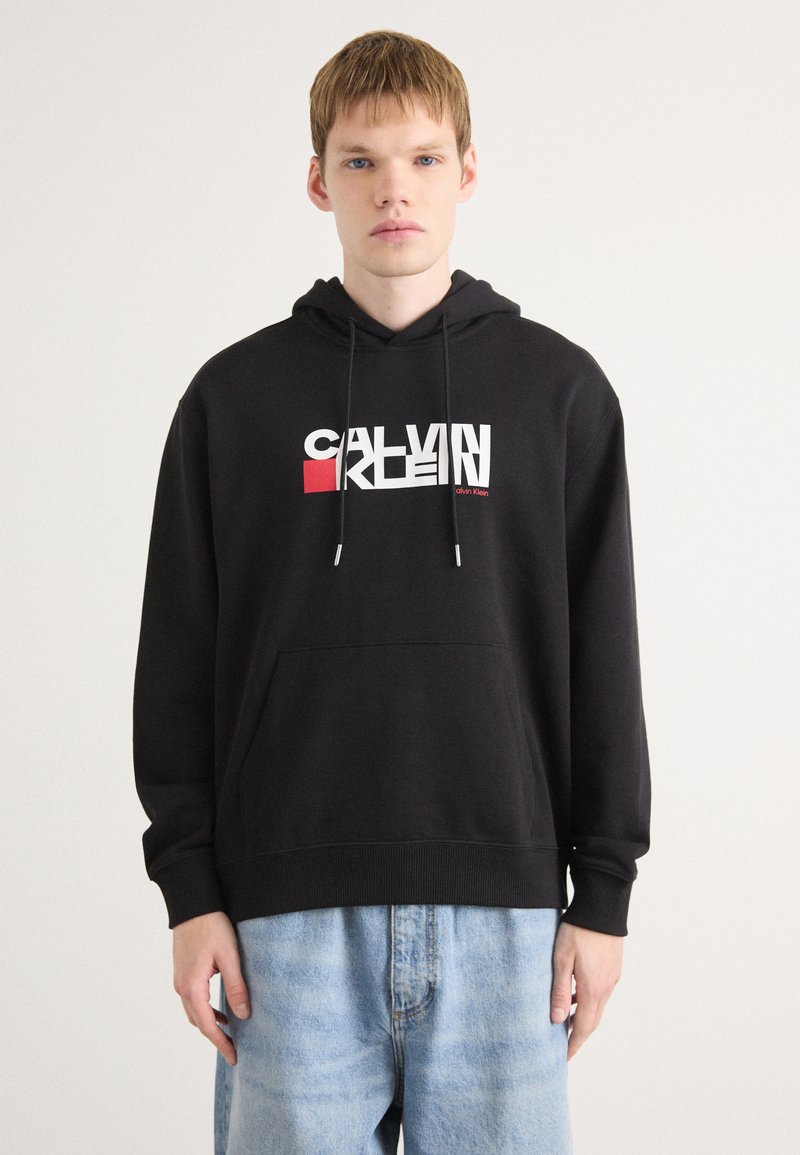 Svart hettegenser med frontlomme, med en flerfarget "CALVIN KLEIN" logo. Laget av myk stoff med en avslappet passform.