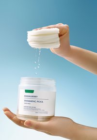 Envase de almohadillas tonificadoras Equalberry para piscina, sostenido con almohadillas blancas en capas arriba, gotas de agua goteando, en un fondo azul claro.