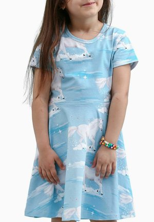 Young girl wearing a blue dress with white horse prints, holding hands in front, and wearing a colorful beaded bracelet on her wrist.
