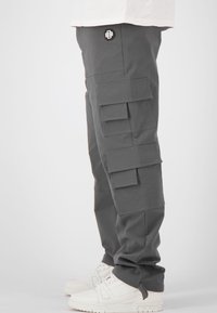 Grijze cargobroek met meerdere voorzakken, een aansluitende pasvorm en verstelbare enkels, gecombineerd met witte sneakers.