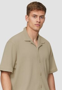 Beige Kurzarmhemd mit einem strukturierten karottenmuster, einem umklappbaren Kragen und Frontknöpfen. Leichtes Material, lässige Passform.