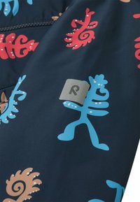 Tissu bleu marine avec des motifs abstraits colorés en rouge, bleu et marron. Comprend une étiquette rectangulaire en argent avec un logo "R" en relief.
