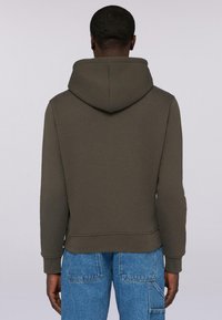 Olivgrön hoodie med dragsko i huvan, ribbade ärmslut och midja. Tillverkad av mjukt material med en något strukturerad yta.