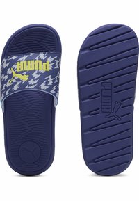 Blå sandaler med texturerad rem som har ett vitt blixtmönster och en gul "Puma"-logotyp. Sulan är präglad med spår för grepp.