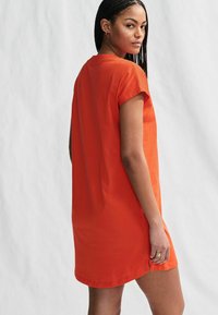 Orange bomulds t-shirt kjole med korte ærmer og en afslappet pasform, der har en buet kant og sideslids for nem bevægelse.