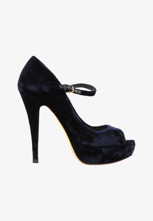 Zapato Mary Jane de terciopelo negro con tacón alto, puntera redondeada, suela con plataforma y correa ajustable en el tobillo con una pequeña hebilla dorada.