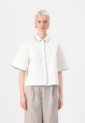 White short-sleeve shirt with a pointed collar, featuring black contrasting stitching along the collar and hem. Smooth cotton fabric.