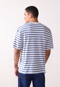Camiseta de rayas que presenta líneas horizontales en azul y blanco, con mangas cortas, cuello redondo y un corte holgado. Fabricada en suave material de algodón.