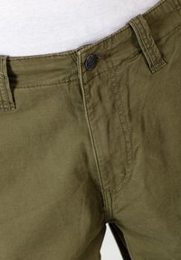 Olivgrüne Baumwollhosen mit einem Knopfverschluss, ausgestattet mit Fronttaschen und sichtbaren Nähdetails. Glatte Textur mit einem lockeren Schnitt.