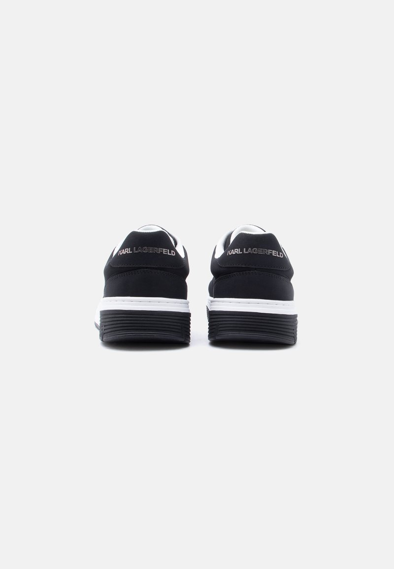 Par de zapatillas negras de Karl Lagerfeld vistas desde atrás, con medias suelas blancas y suelas gruesas negras sobre un fondo liso.