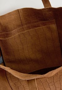Braune Wildleder-Tasche mit einer strukturierten Innenauskleidung im Krokodilmuster. Das Innere weist sichtbare Nähte und eine weiche Oberfläche auf.