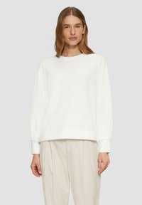 Witte sweatshirt met een ronde halslijn, lange pofmouwen en geribbelde manchetten, gecombineerd met lichtbeige broek. Zachte textuur.