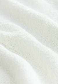 Tissu tricoté blanc avec une surface douce et texturée, présentant un subtil motif de fils entrelacés et de douces vagues.