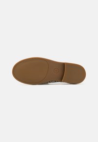 Semelle en caoutchouc marron d'une chaussure plate avec une adhérence texturée, marquage Michael Kors près des orteils et logo MK au niveau de la semelle intermédiaire.
