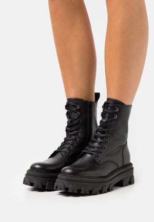 Schwarze Leder-Stiefeletten mit Schnürung, seitlichem Reißverschluss, klobiger Gummisohle und strukturierter Oberfläche, mit abgerundeter Spitze und verstärkten Akzenten.