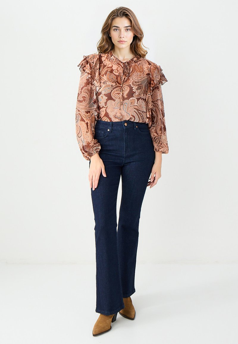 Bluzka w kwiatowy wzór paisley z falbanastymi rękawami, zestawiona z ciemnoniebieskimi dżinsami z wysokim stanem i brązowymi zamszowymi botkami do kostek.