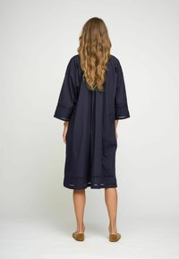 Navyblaues Baumwollkleid mit weiten Ärmeln und knielangem Schnitt; verfügt über einen zarten Spitzenbesatz entlang des Saums und der Ärmel.