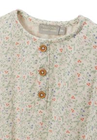 Chemise à manches courtes en tissu crème ornée d'un imprimé floral vert, rose et bleu, avec trois boutons en bois au niveau du col.