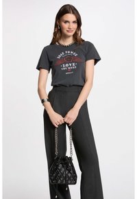 T-shirt graphique noir avec un motif d'ailes, porté avec un pantalon gris taille haute. Accessoirisé avec un sac seau noir matelassé et une chaîne en argent.