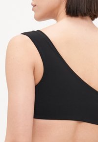 Čierny bezrukávový top s hlbokým výstrihom na chrbte. Vyrobený z hladkého, elastického materiálu. Obsahuje široké ramenné popruhy a priliehavý strih.