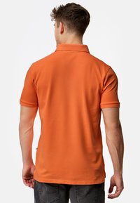 Oranje polo met een kraag en korte mouwen, gemaakt van textuurstof. Getailleerde pasvorm met zichtbare naden en stiksels.