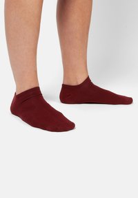 Bordeaux ankelstrømper lavet af blødt stof, med en glat tekstur og et enkelt design, der dækker foden og anklen.