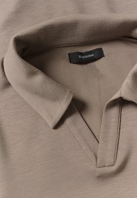 Cuello de polo en taupe suave con una etiqueta negra "Matinique" cosida en el interior del escote, tejido ligeramente texturizado.