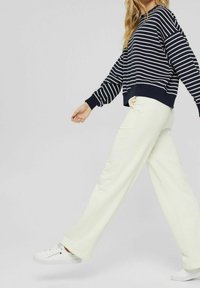 Sweat-shirt rayé bleu marine et blanc avec une coupe décontractée; associé à un pantalon large couleur crème et des baskets blanches. Tissu doux, design décontracté.