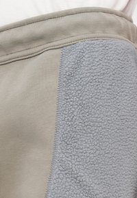 Világosszürke melegítónadrág puha fleece oldalsó panelek béléssel és rugalmas derékkal; sima textúra varrási részletekkel a varrat mentén.