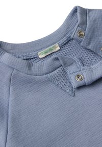 Světle modrý pletený kousek oděvu se zapínáním na cvoky a štítkem "United Colors of Benetton" přišitým uvnitř.