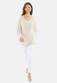 Pulover bej tricotat cu decolteu în formă de V și mâneci lungi, asociat cu pantaloni albi și pantofi bej, având o croială lejeră și o textură ribbed.