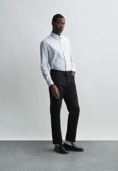 Cămașă cu dungi albă și albastră, asortată cu pantaloni negri drepti și pantofi negri. Material neted cu guler standard.