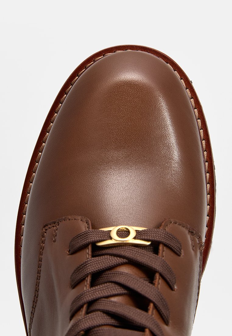 Braunes Leder-Schuh mit einer glatten, glänzenden Oberfläche. Verfügt über tonale Schnürsenkel, einen goldenen Akzent und eine genähte Sohle. Nahaufnahme der Zehenpartie.