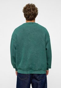 Groene oversized sweatshirt met een ronde hals, verlaagde schouders en geribde manchetten. Zacht materiaal met een licht gebrushte textuur.