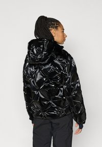 Μαύρο μπουφάν τύπου puffer με γυαλιστερό φινίρισμα, διαθέτει κουκούλα και γεωμετρικό σχέδιο με καπιτονέ. Το ύφασμα φαίνεται λαμπερό και ομαλό.