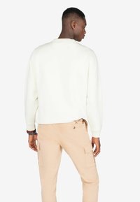 Kremowy sweatshirt o luźnym kroju, z ściągaczami na rękawach i okrągłym dekoltem, zestawiony z lekkimi, jasnobeżowymi spodniami cargo z bocznymi kieszeniami.