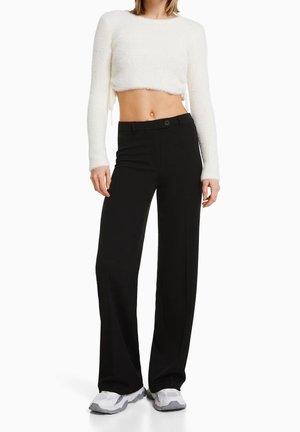 Witte geknipte fuzzy trui met lange mouwen, gecombineerd met hoge zwarte wijde broek en witte sneakers.