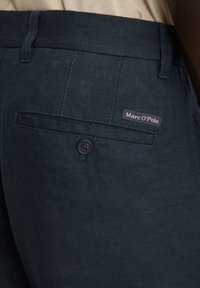 Donkergroene linnen broek met een achterzak met een enkele knop en een merklabel met "Marc O'Polo" ter identificatie.