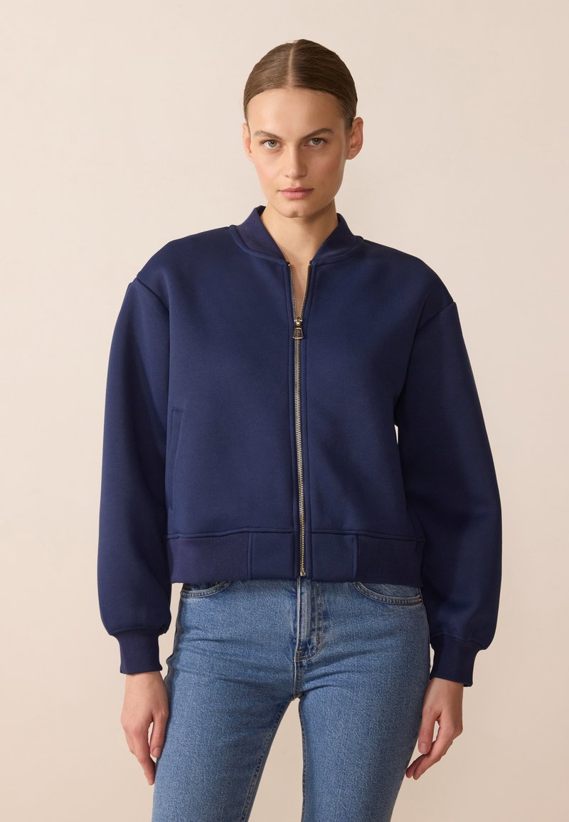 Sweatshirt zippé bleu marine, avec un col haut, des poignets et un ourlet côtelés, des poches latérales et une coupe décontractée. Fabriqué en tissu doux.
