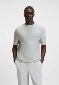 Light grey short-sleeve knitted sweater with a round neckline and small black "BOSS" logo on the chest, worn with light-colored trousers.
