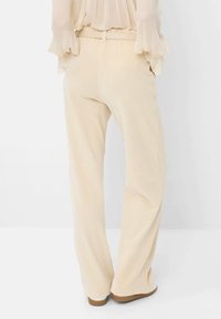 Pantalons en velours côtelé beige clair avec une coupe large, présentant un tissu texturé et une taille ajustée. Tissu doux et détails matériels minimalistes.