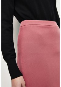 Roze aansluitende rok van gestructureerde stof, met een hoge taille en zijnaadaccenten, gecombineerd met een zwart top met lange mouwen.