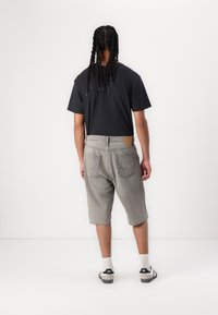 Pantalones cortos de mezclilla gris con un corte recto, que cuentan con un parche trasero y dos bolsillos traseros. Llevado con una camiseta negra y calcetines blancos.